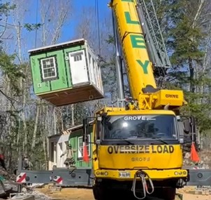 Photo of a crane lifting a manufactured ADU into place on a cleared piece of land